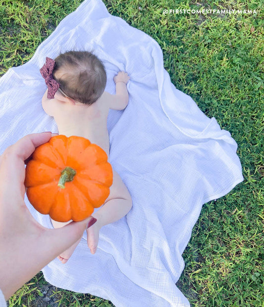 Baby crawling in grass and hand holding small pumpkin